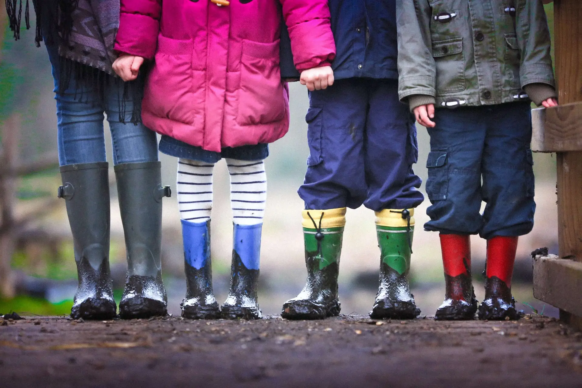 four kids standing outside with mud on their rain boots