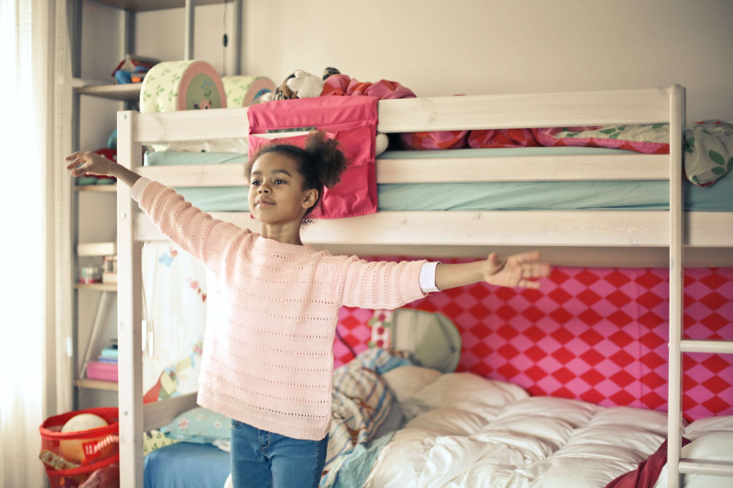 girl wearing a pink sweater and jeans dancing in her bedroom