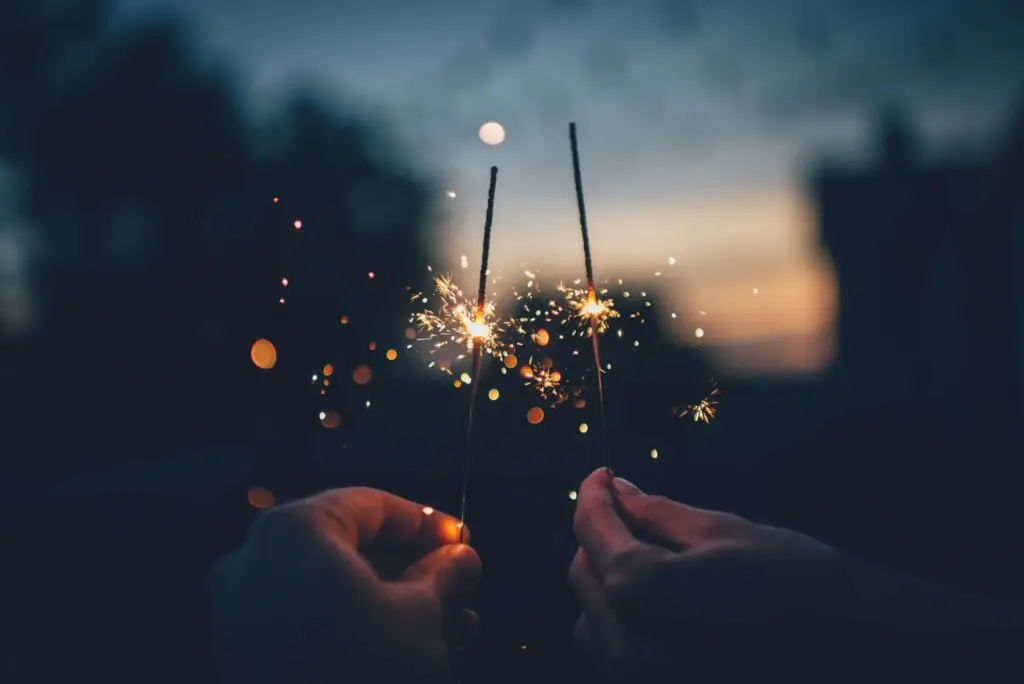 two people holding a half burned sparkler outside in the evening