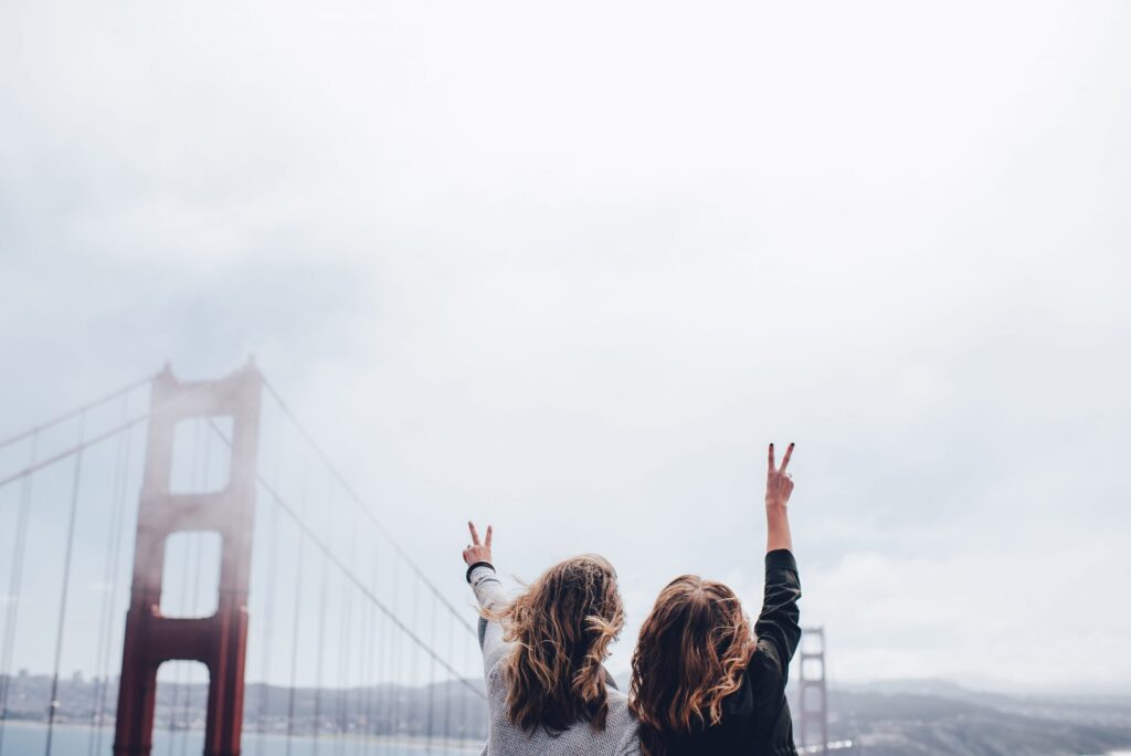 two girls using the peace sign next to the golden gate bridge