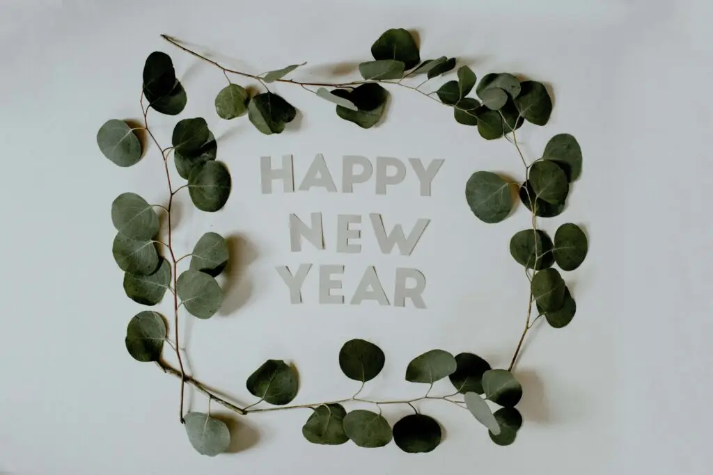 happy new year cut out of paper placed on wall surrounded by green leaves