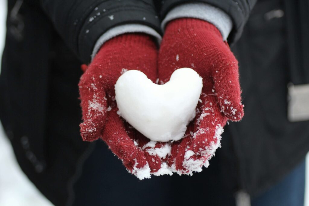 person holding a heart shaped snowball in their hands