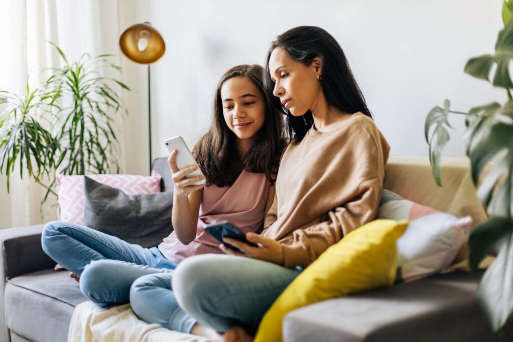 mom and daughter sitting on a couch together looking at a smartphone