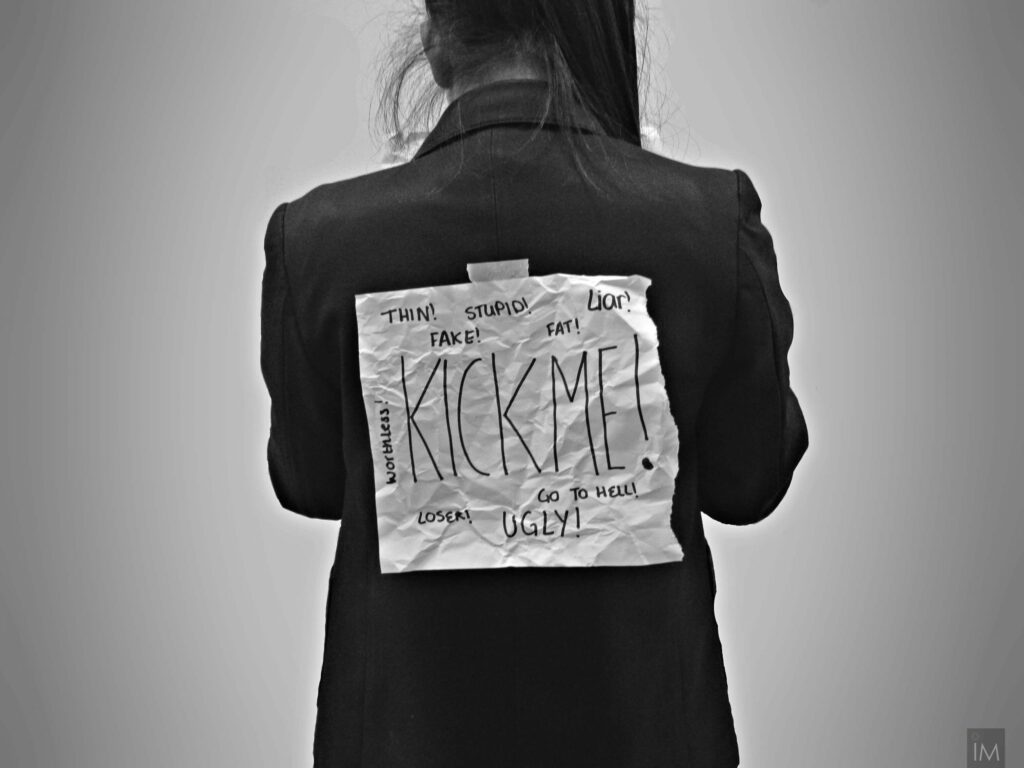 person with paper taped to their back with insults written on it