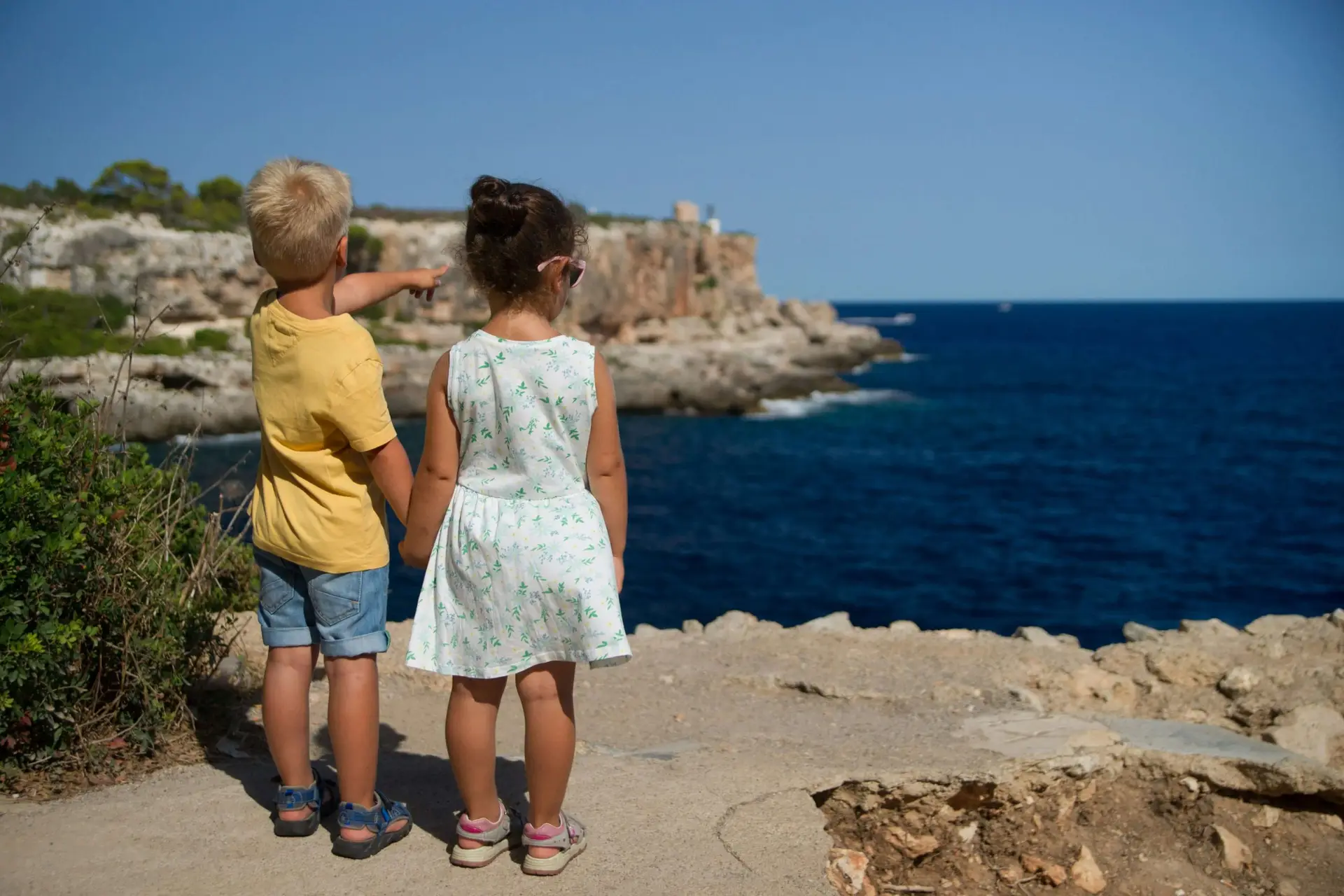 little boy and girl holding hands pointing at the ocean