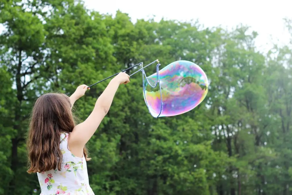 girl making big bubbles outside with bubble maker