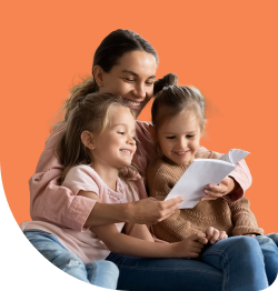 A woman is sitting with two young children on her lap, reading a book together. They are all smiling, creating a warm and joyful atmosphere. The background is a solid orange color.