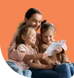 A woman is sitting with two young children on her lap, reading a book together. They are all smiling, creating a warm and joyful atmosphere. The background is a solid orange color.