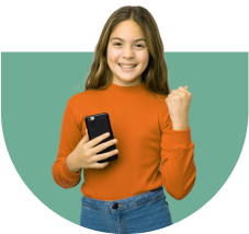 A young girl with long hair smiles and holds a smartphone in one hand while making a fist with the other. She wears an orange long-sleeve shirt and blue jeans, standing against a green semi-circle background.