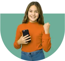 A young girl with long hair smiles and holds a smartphone in one hand while making a fist with the other. She wears an orange long-sleeve shirt and blue jeans, standing against a green semi-circle background.