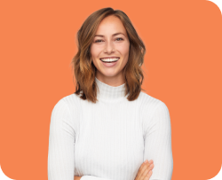 A smiling woman with shoulder-length hair is wearing a white turtleneck sweater and standing with her arms crossed. The background is a solid orange color.