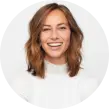 A woman with shoulder-length brown hair is smiling in a headshot. She is wearing a white turtleneck sweater and is set against a plain white background.