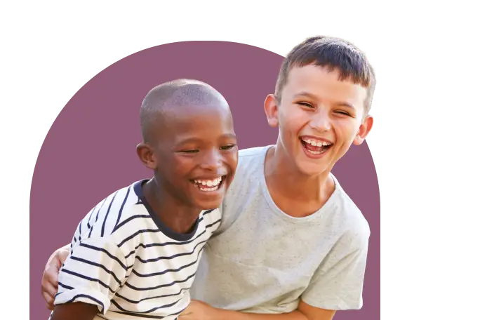 Two boys laughing joyfully, one wearing a striped shirt and the other in a gray t-shirt, with a maroon semi-circular background. They appear to be having fun together.