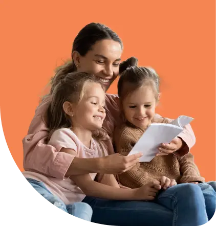 A woman happily reads a book with two young girls sitting on her lap against an orange background. They all appear engaged and joyful.