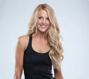 A person with long, wavy blonde hair and a black tank top smiles against a plain background.