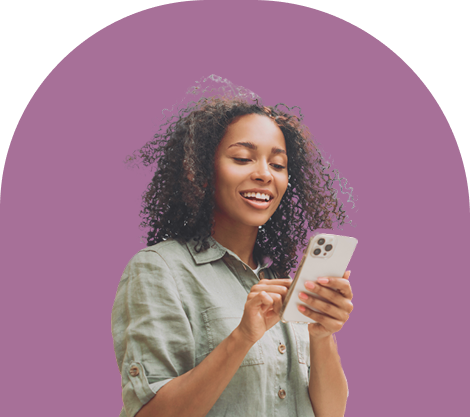 A smiling woman with curly hair wearing a light green button-up shirt looks at and interacts with her smartphone, standing against a solid purple background.