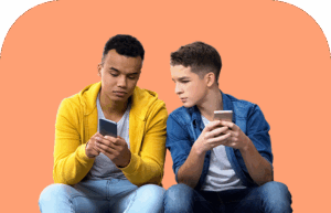 Two teenage boys sitting side by side, each holding a smartphone. One boy in a yellow hoodie looks at his phone, while the boy in a denim shirt leans in, appearing curious about the other’s screen. Orange background.