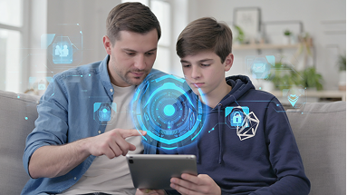 A man and a boy sit on a couch using a tablet together, with blue digital security interface graphics superimposed, suggesting a focus on cybersecurity or safe technology use.