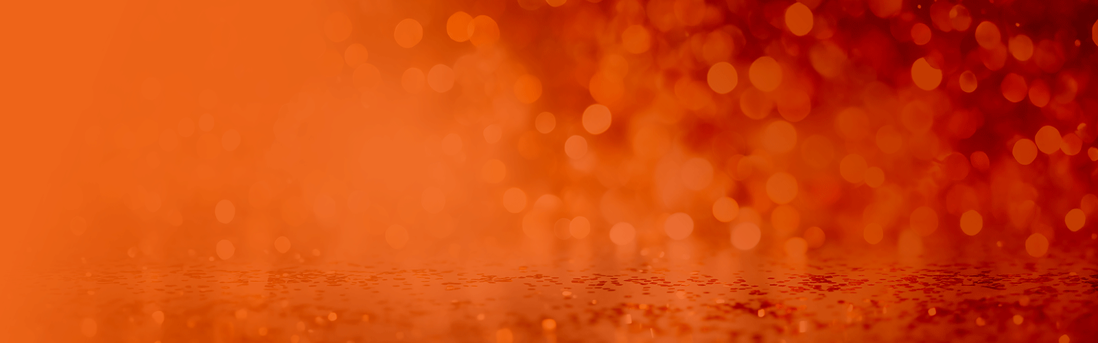 A blurred orange background with soft, glowing bokeh lights and subtle specks, creating a warm, festive, and abstract effect.