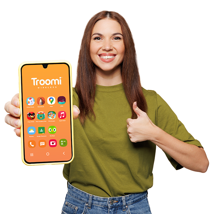 A smiling woman in a green shirt holds a large smartphone displaying the Troomi Wireless home screen and gives a thumbs-up gesture with her other hand.