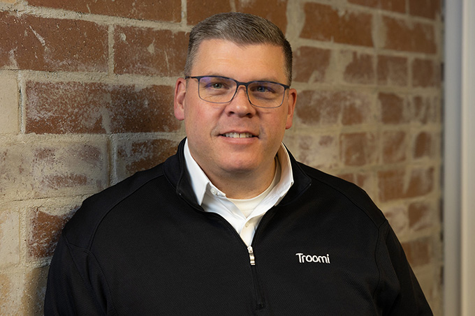 Troomi CEO Bill Brady stands smiling against a brick wall